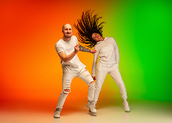 Image showing Stylish sportive caucasian couple dancing hip-hop on colorful gradient background at dance hall in neon light.