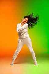 Image showing Stylish sportive caucasian woman dancing hip-hop on colorful gradient background at dance hall in neon light.