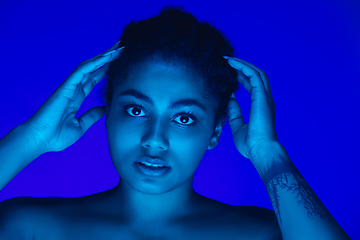 Image showing Beautiful african-american woman portrait isolated on blue studio background in neon light, monochrome