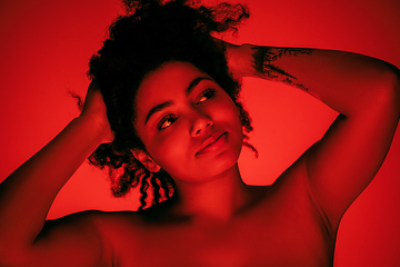 Image showing Beautiful african-american woman portrait isolated on red studio background in neon light, monochrome