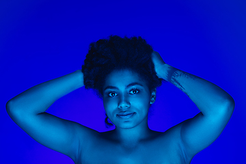 Image showing Beautiful african-american woman portrait isolated on blue studio background in neon light, monochrome