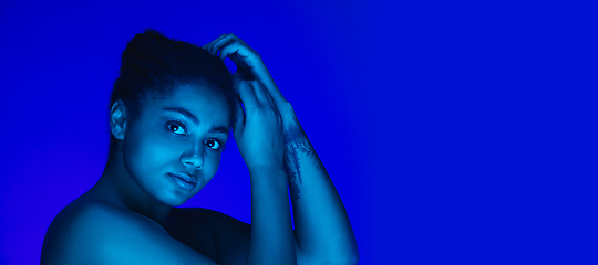 Image showing Beautiful african-american woman portrait isolated on blue studio background in neon light, monochrome