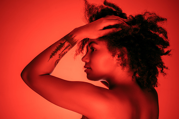 Image showing Beautiful african-american woman portrait isolated on red studio background in neon light, monochrome