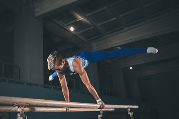 Image showing Little male gymnast training in gym, flexible and active. Caucasian fit little boy, athlete in sportswear practicing in exercises for strength, balance.