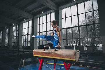 Image showing Little male gymnast training in gym, flexible and active. Caucasian fit little boy, athlete in sportswear practicing in exercises for strength, balance.