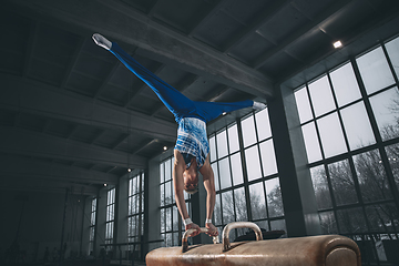 Image showing Little male gymnast training in gym, flexible and active. Caucasian fit little boy, athlete in sportswear practicing in exercises for strength, balance.