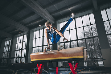 Image showing Little male gymnast training in gym, flexible and active. Caucasian fit little boy, athlete in sportswear practicing in exercises for strength, balance.