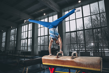 Image showing Little male gymnast training in gym, flexible and active. Caucasian fit little boy, athlete in sportswear practicing in exercises for strength, balance.