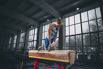 Image showing Little male gymnast training in gym, flexible and active. Caucasian fit little boy, athlete in sportswear practicing in exercises for strength, balance.