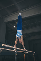 Image showing Little male gymnast training in gym, flexible and active. Caucasian fit little boy, athlete in sportswear practicing in exercises for strength, balance.