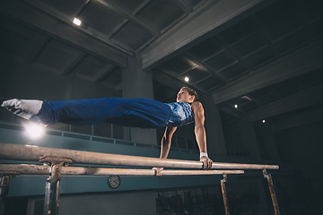 Image showing Little male gymnast training in gym, flexible and active. Caucasian fit little boy, athlete in sportswear practicing in exercises for strength, balance.