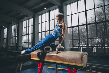 Image showing Little male gymnast training in gym, flexible and active. Caucasian fit little boy, athlete in sportswear practicing in exercises for strength, balance.