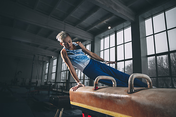 Image showing Little male gymnast training in gym, flexible and active. Caucasian fit little boy, athlete in sportswear practicing in exercises for strength, balance.