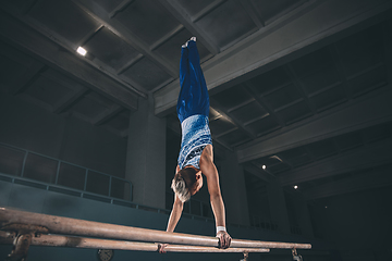 Image showing Little male gymnast training in gym, flexible and active. Caucasian fit little boy, athlete in sportswear practicing in exercises for strength, balance.