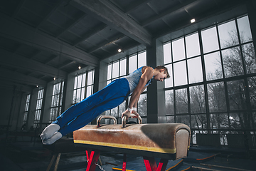 Image showing Little male gymnast training in gym, flexible and active. Caucasian fit little boy, athlete in sportswear practicing in exercises for strength, balance.