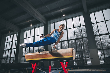 Image showing Little male gymnast training in gym, flexible and active. Caucasian fit little boy, athlete in sportswear practicing in exercises for strength, balance.