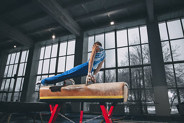 Image showing Little male gymnast training in gym, flexible and active. Caucasian fit little boy, athlete in sportswear practicing in exercises for strength, balance.