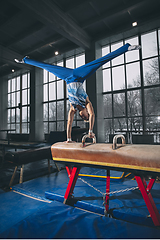 Image showing Little male gymnast training in gym, flexible and active. Caucasian fit little boy, athlete in sportswear practicing in exercises for strength, balance.