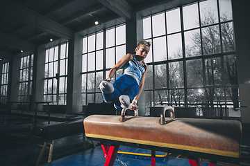 Image showing Little male gymnast training in gym, flexible and active. Caucasian fit little boy, athlete in sportswear practicing in exercises for strength, balance.