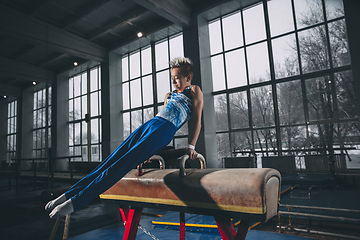 Image showing Little male gymnast training in gym, flexible and active. Caucasian fit little boy, athlete in sportswear practicing in exercises for strength, balance.