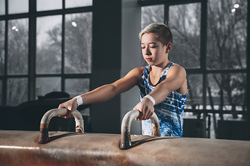 Image showing Little male gymnast training in gym, flexible and active. Caucasian fit little boy, athlete in sportswear practicing in exercises for strength, balance.