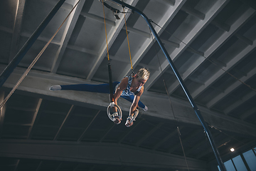 Image showing Little male gymnast training in gym, flexible and active. Caucasian fit little boy, athlete in sportswear practicing in exercises for strength, balance.