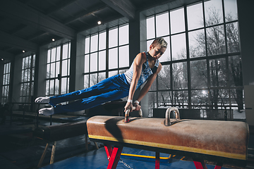 Image showing Little male gymnast training in gym, flexible and active. Caucasian fit little boy, athlete in sportswear practicing in exercises for strength, balance.