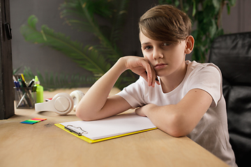 Image showing Little boy sitting at the table during listening to teacher on online videocall, educational course