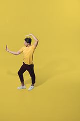 Image showing High angle view of young man on yellow studio background. Boy in motion, jumping high. Human emotions and facial expressions concept