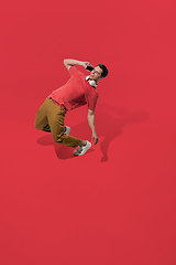 Image showing High angle view of young man on red studio background. Boy in motion, jumping high. Human emotions and facial expressions concept