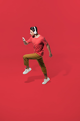 Image showing High angle view of young man on red studio background. Boy in motion, jumping high. Human emotions and facial expressions concept