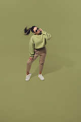 Image showing High angle view of young woman on green studio background. Girl in motion or movement. Human emotions and facial expressions concept