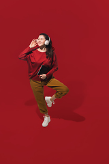 Image showing High angle view of young woman on red studio background. Girl in motion or movement. Human emotions and facial expressions concept