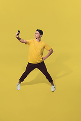 Image showing High angle view of young man on yellow studio background. Boy in motion, jumping high. Human emotions and facial expressions concept