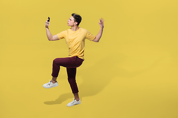 Image showing High angle view of young man on yellow studio background. Boy in motion, jumping high. Human emotions and facial expressions concept