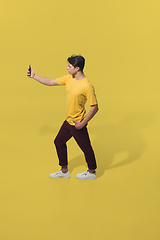 Image showing High angle view of young man on yellow studio background. Boy in motion, jumping high. Human emotions and facial expressions concept