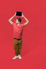 Image showing High angle view of young man on red studio background. Boy in motion, jumping high. Human emotions and facial expressions concept