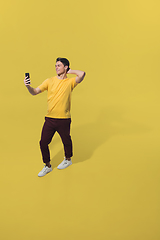 Image showing High angle view of young man on yellow studio background. Boy in motion, jumping high. Human emotions and facial expressions concept