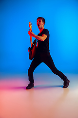 Image showing Young caucasian musician playing guitar in neon light on blue background, inspired