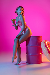 Image showing Beautiful girl in fashionable swimsuit isolated on gradient studio background in neon light. Summer, resort, fashion and weekend concept