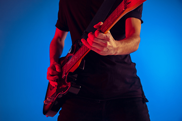 Image showing Young caucasian musician playing guitar in neon light on blue background, inspired