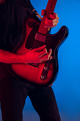 Image showing Young caucasian musician playing guitar in neon light on blue background, inspired