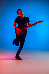 Image showing Young caucasian musician playing guitar in neon light on blue background, inspired