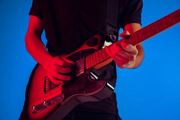 Image showing Young caucasian musician playing guitar in neon light on blue background, inspired