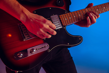 Image showing Young caucasian musician playing guitar in neon light on blue background, inspired