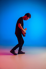 Image showing Young caucasian musician playing guitar in neon light on blue background, inspired