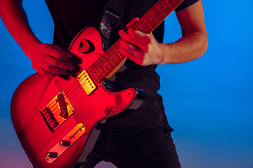 Image showing Young caucasian musician playing guitar in neon light on blue background, inspired