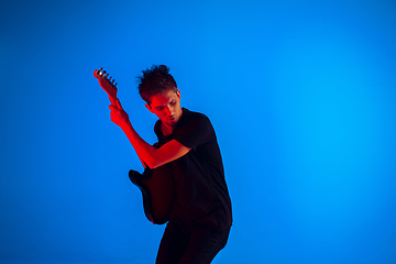 Image showing Young caucasian musician playing guitar in neon light on blue background, inspired