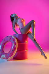 Image showing Beautiful girl in fashionable swimsuit isolated on gradient studio background in neon light. Summer, resort, fashion and weekend concept