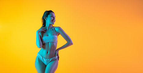 Image showing Fashion portrait of seductive girl in stylish swimwear posing on a bright yellow background. Summertime, beach season